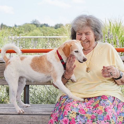 Eine lachende Bewohnerin mit ihrem Hund im Garten der Mühlehalde, sie sitzt auf einer Bank und spielt mit ihrem Haustier.