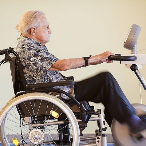 Eine Bewohnerin sitzt im Rollstuhl vor einem Therapiegerät und führt Übungen aus, um ihre Beweglichkeit zu erhalten.