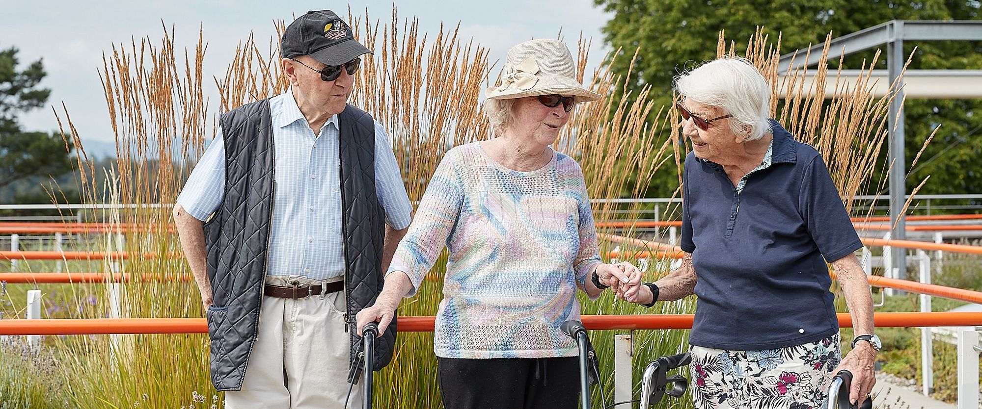 Ein Senior mit Mütze und zwei gut gelaunte Bewohnerinnen im Garten der Mühlehalde im angeregten Gespräch.