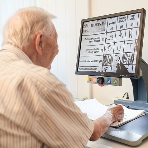 Ein sehbehinderter Bewohner der Mühlehalde löst begeistert Kreuzworträtsel über einen Bildschirm, der die Papiervorlage des Rätsel gross und kontrastreich darstellt.