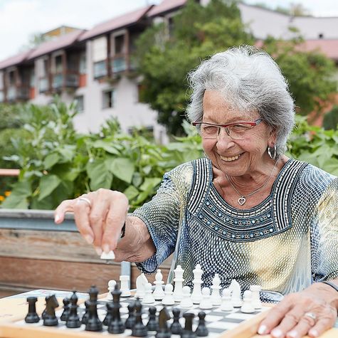 Eine Bewohnerin sitzt im Garten, lacht fröhlich und spielt Schach.